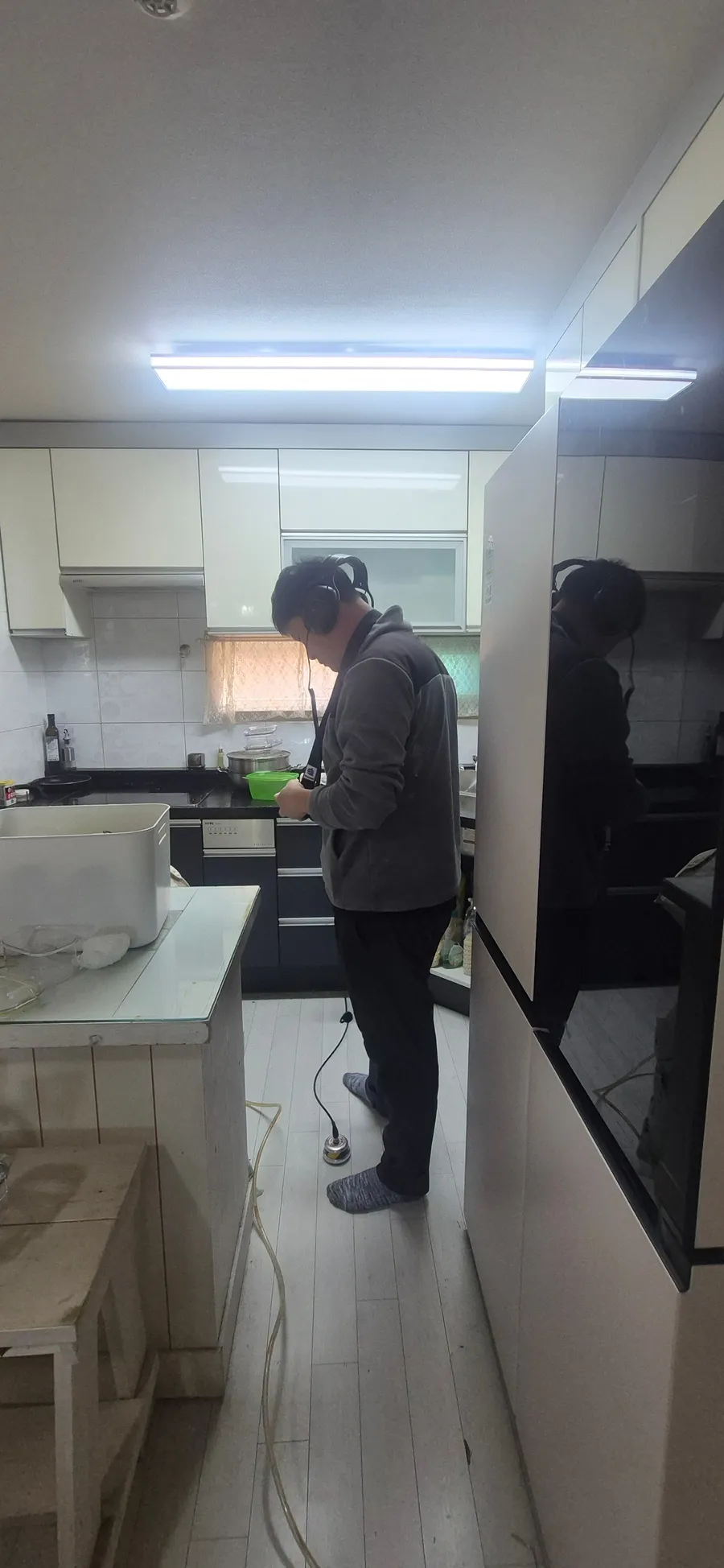 주방에서 청음 장비로 바닥 아래 물소리를 듣는 모습